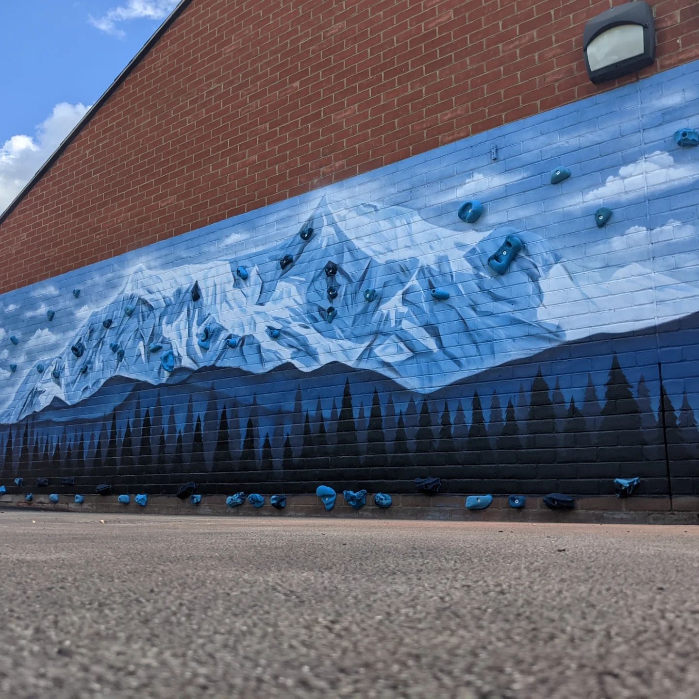 Mural of a snowy mountain range and dark forest painted on a brick building with climbing holds.