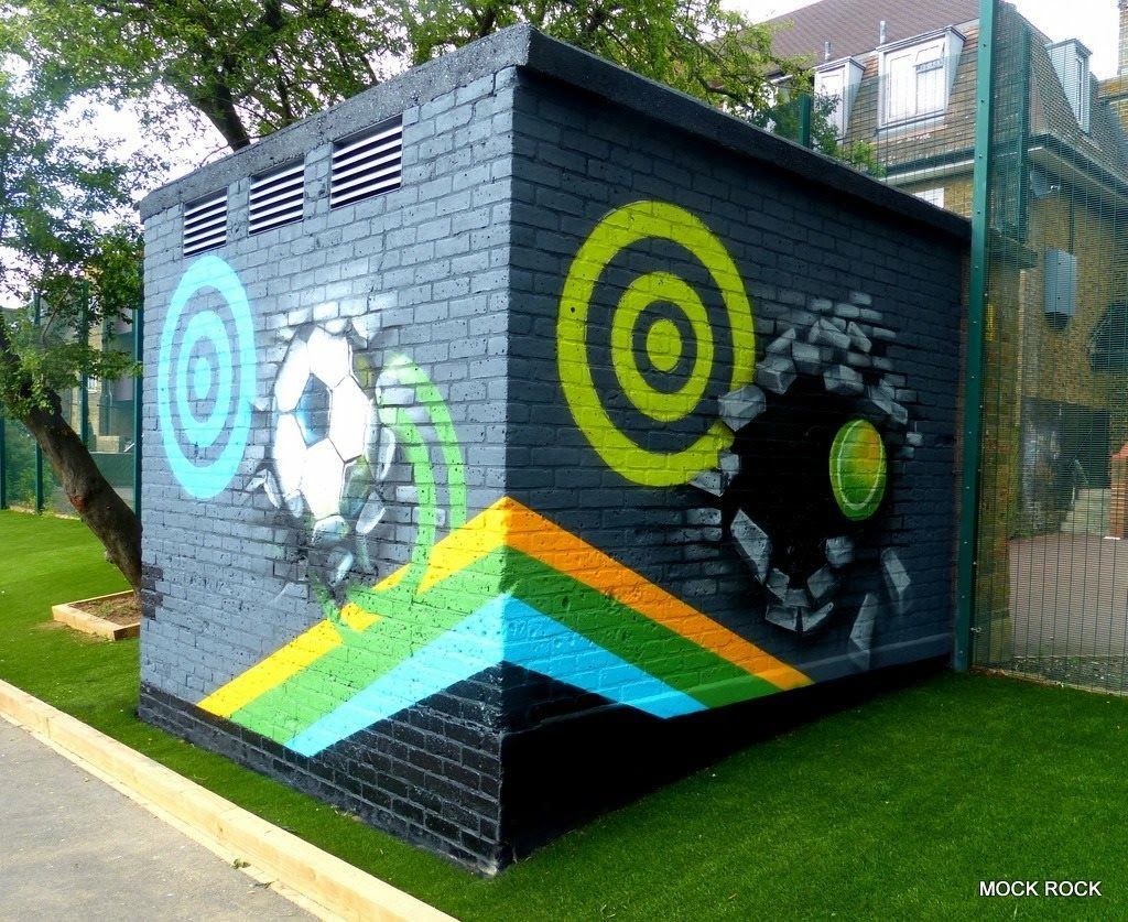 Colorful graffiti art on a brick building; soccer ball breaking through, concentric circles, and geometric lines.