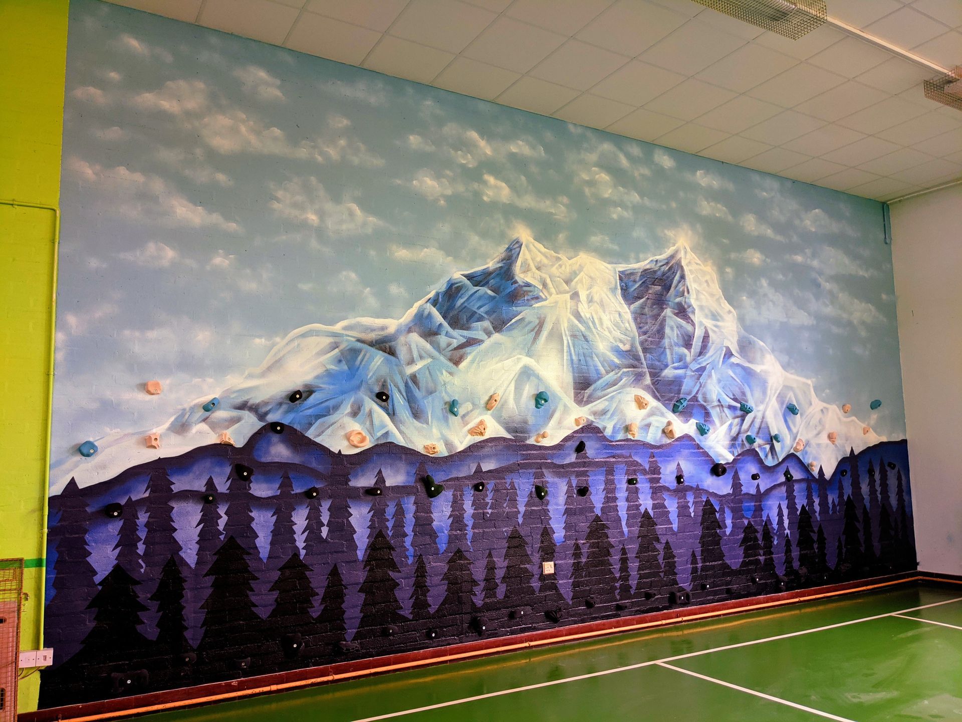 Mural of snowy mountains with a dark forest at the base, painted on a wall in a room.