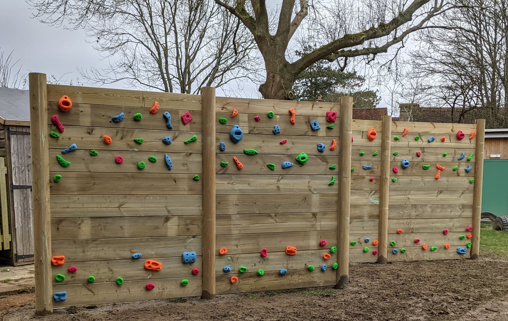 Wooden climbing wall with colorful handholds in a grassy area.