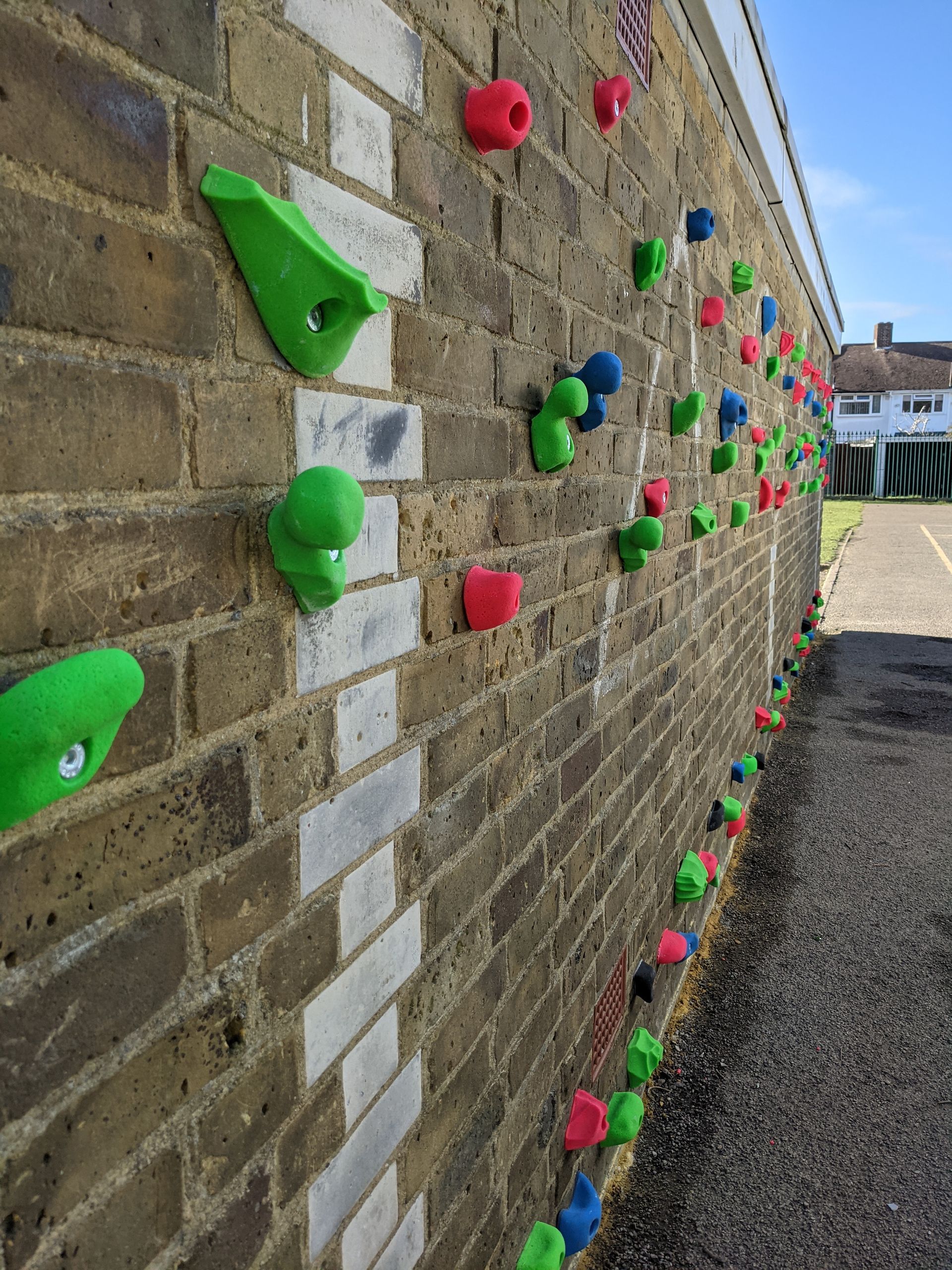 Climbing wall with colorful holds on a brick wall outdoors.