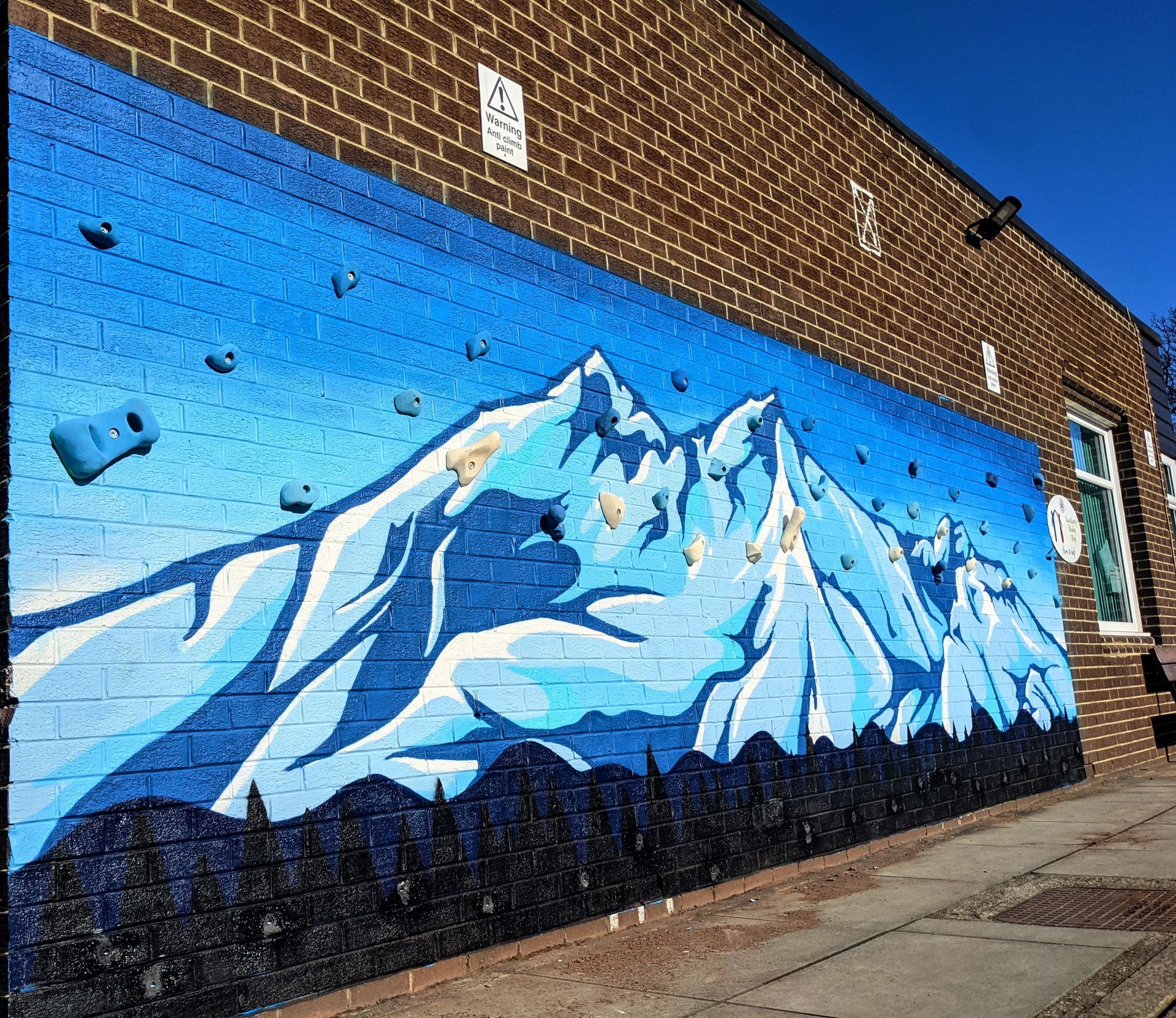 Mural of blue and white mountains on a brick wall, with climbing holds installed.