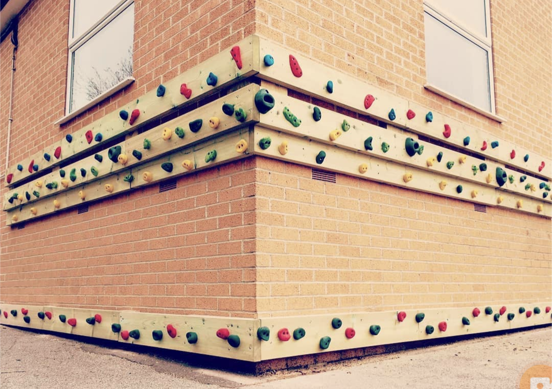 Corner brick wall with wooden climbing holds in red, green, and tan.