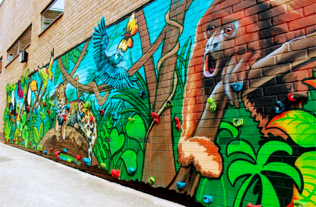 Colorful jungle mural on brick wall with parrots, leopard, and monkey.
