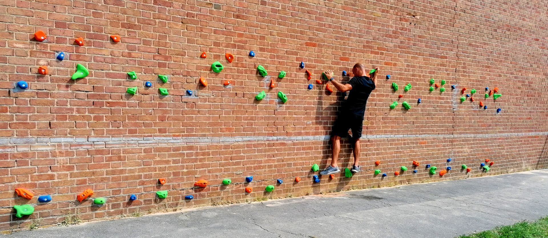 A person climbing a brick wall with colorful holds. The person is reaching upwards.