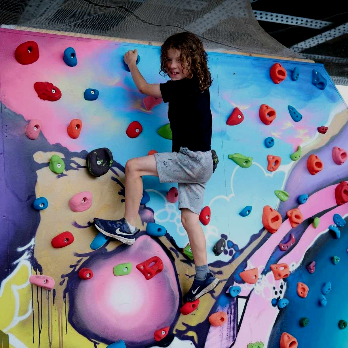 Young person climbing a colorful rock wall, smiling.