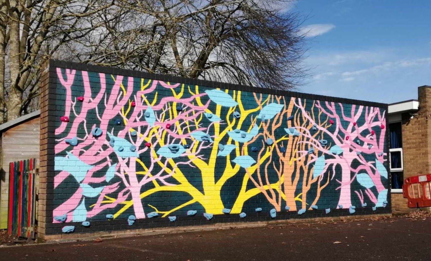 Colorful mural of stylized trees on a brick wall, blue birds and leaves, against a dark blue background.