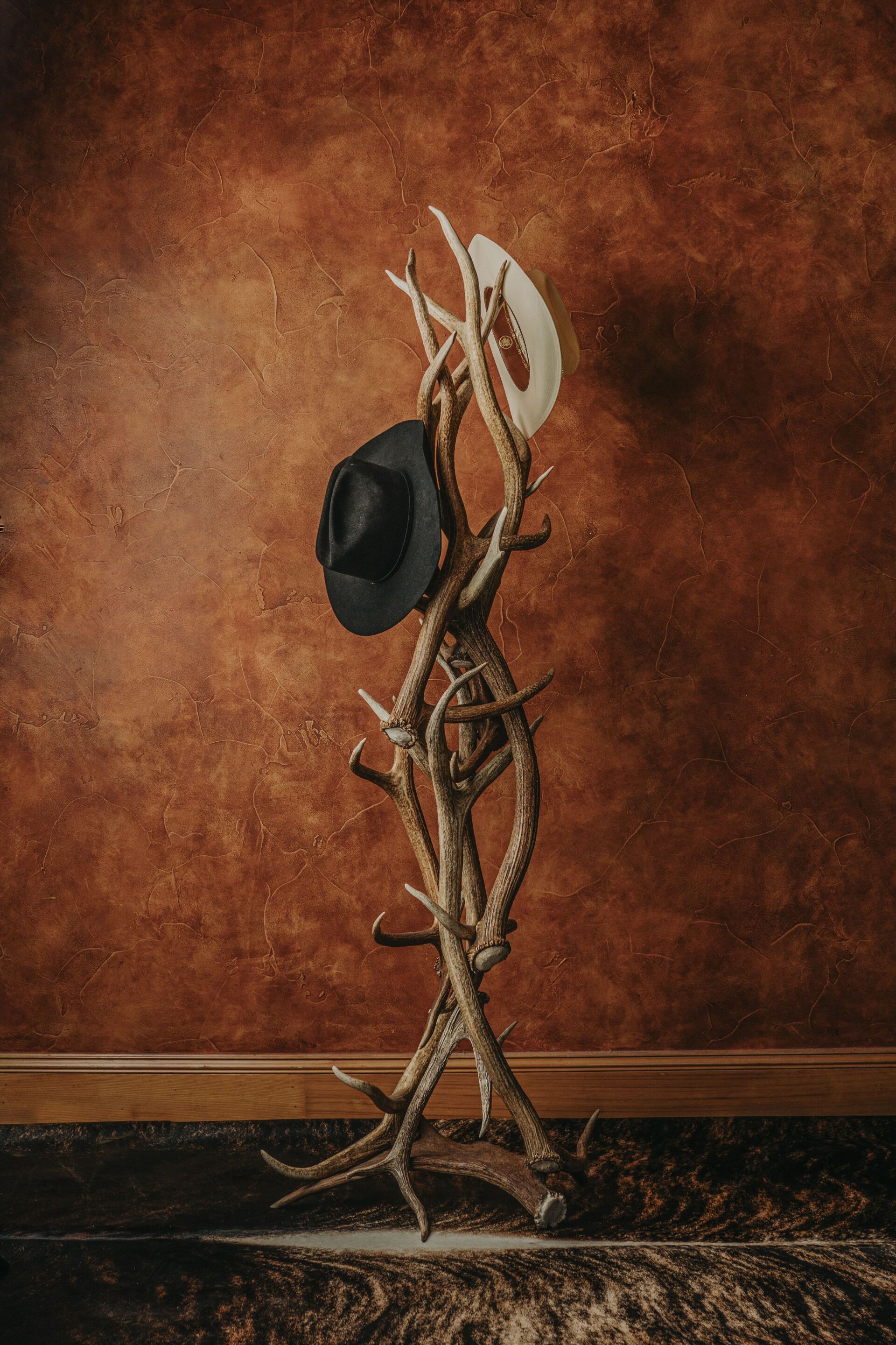 A hat rack made of deer antlers with two hats hanging from it.