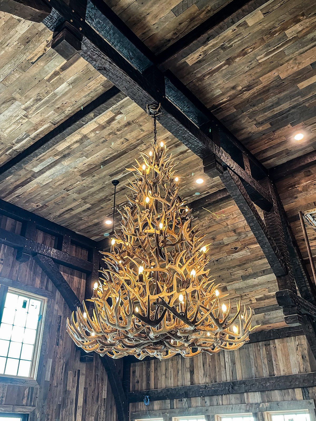 A large chandelier made of antlers is hanging from the ceiling of a wooden building.
