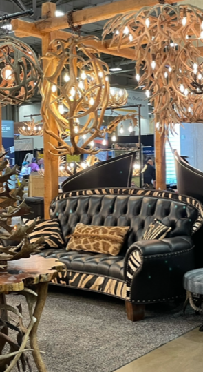 A black leather couch with zebra print pillows is sitting in a room with antlers hanging from the ceiling.