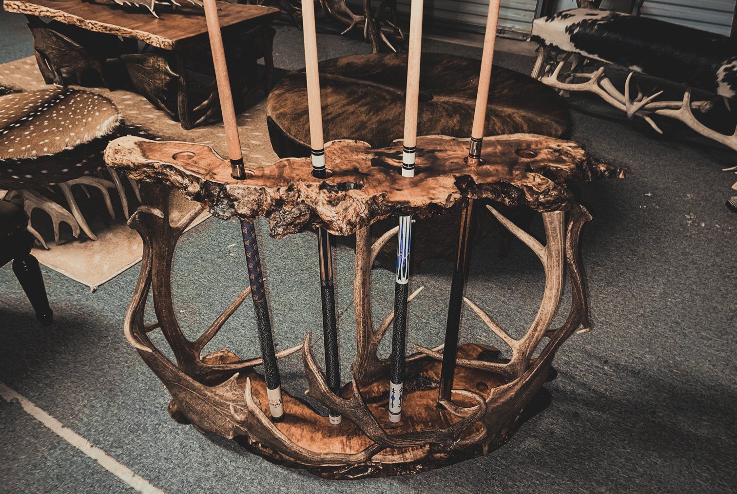 A cue rack made out of antlers is sitting on a carpeted floor.