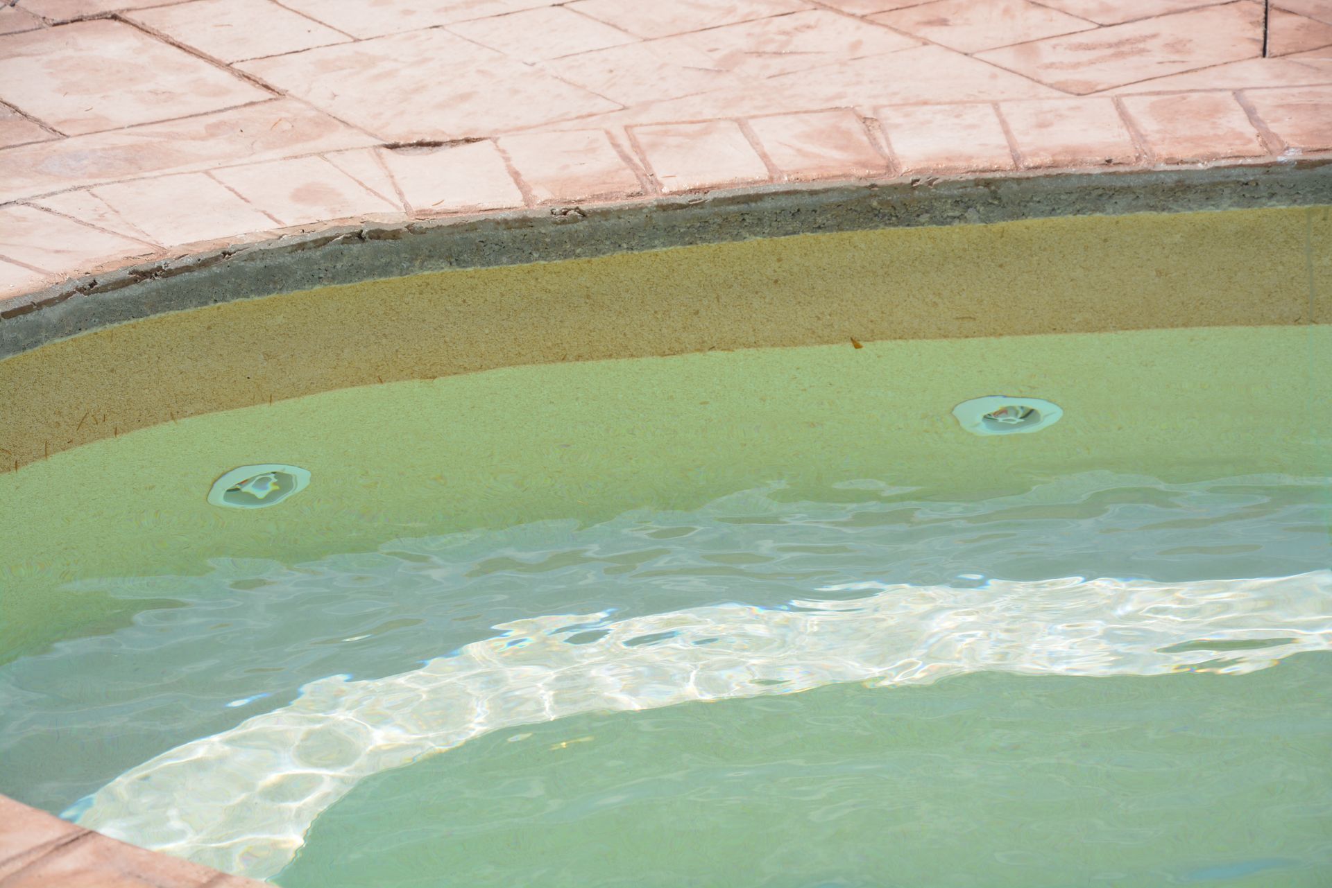 Vista a bordo piscina con acqua limpida, sedie a sdraio e ulivi sotto un cielo azzurro brillante. Statua in primo piano.