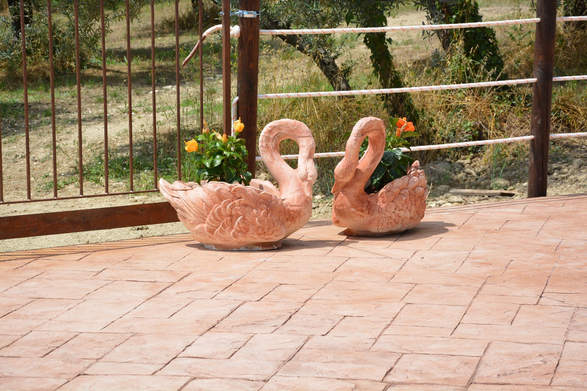 Due fioriere a forma di cigno piene di fiori su un patio in mattoni, vicino a una recinzione.