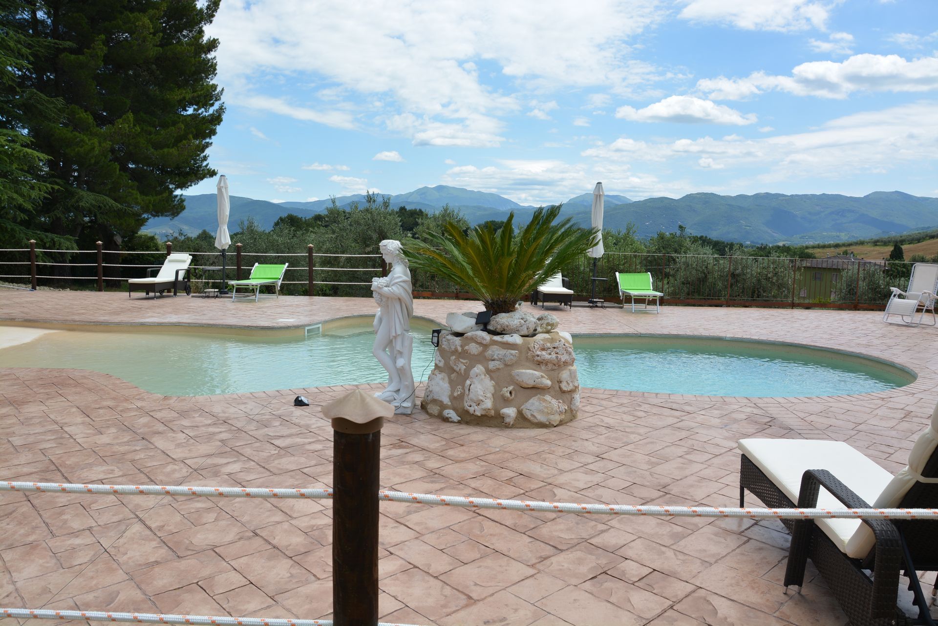 Piscina con vista sulle montagne; sedie a sdraio, scultura, giornata di sole.