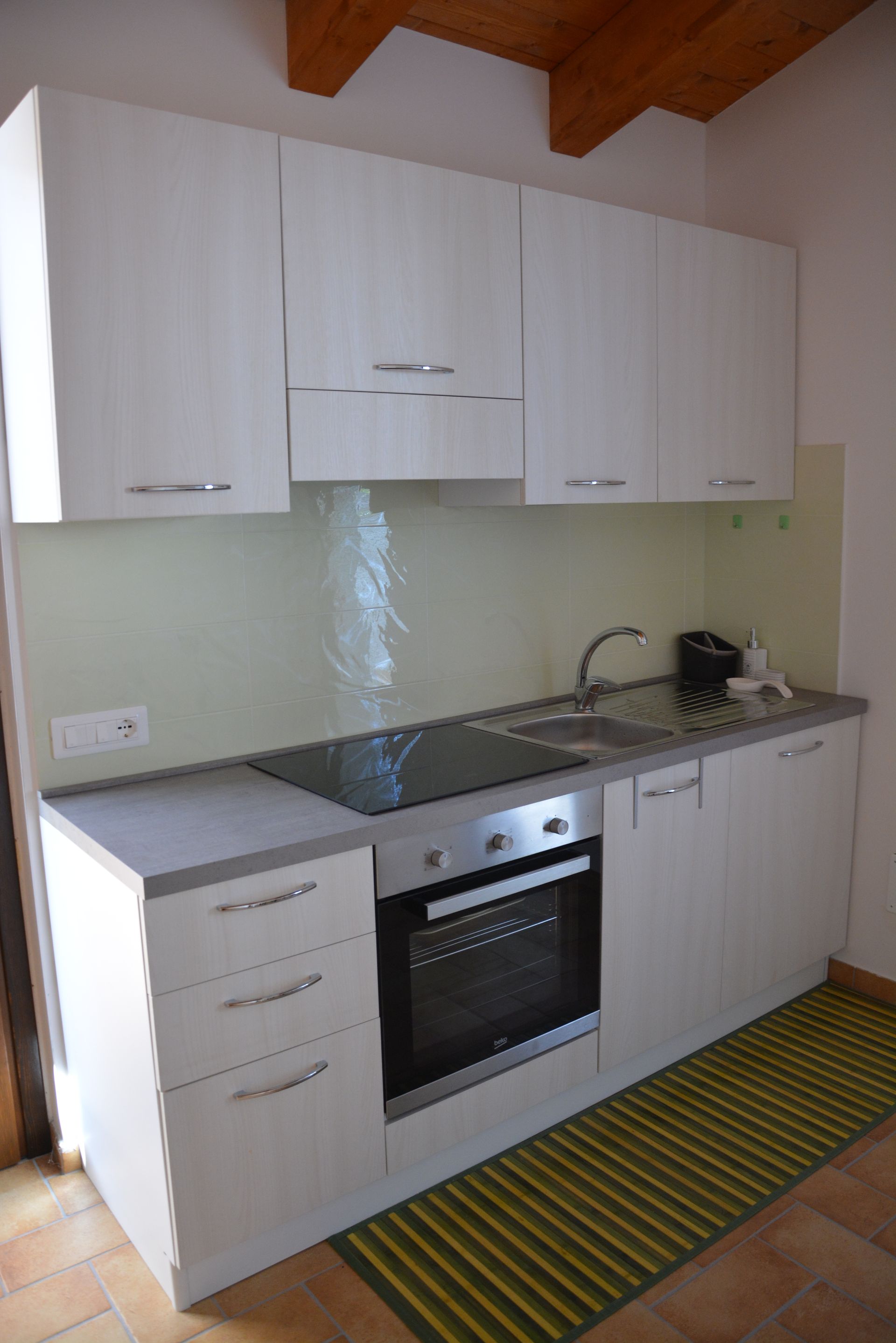 Cucina bianca con pensili, piano cottura, lavello e piano di lavoro. Tappeto a righe gialle e nere.