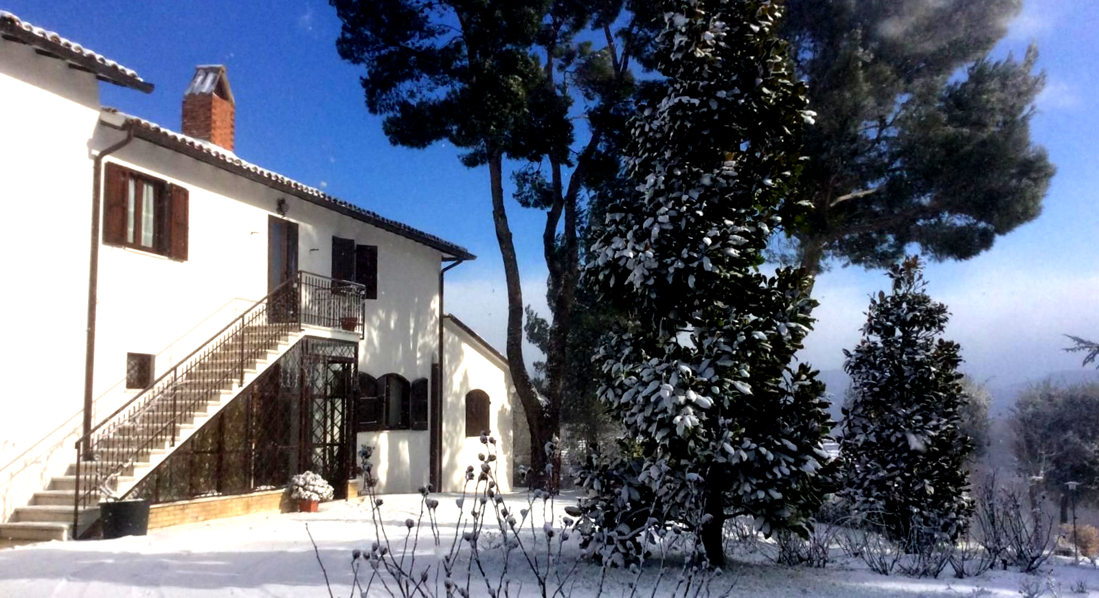 Dolci colline verdi e montagne in lontananza sotto un cielo nuvoloso, con una casa in primo piano.