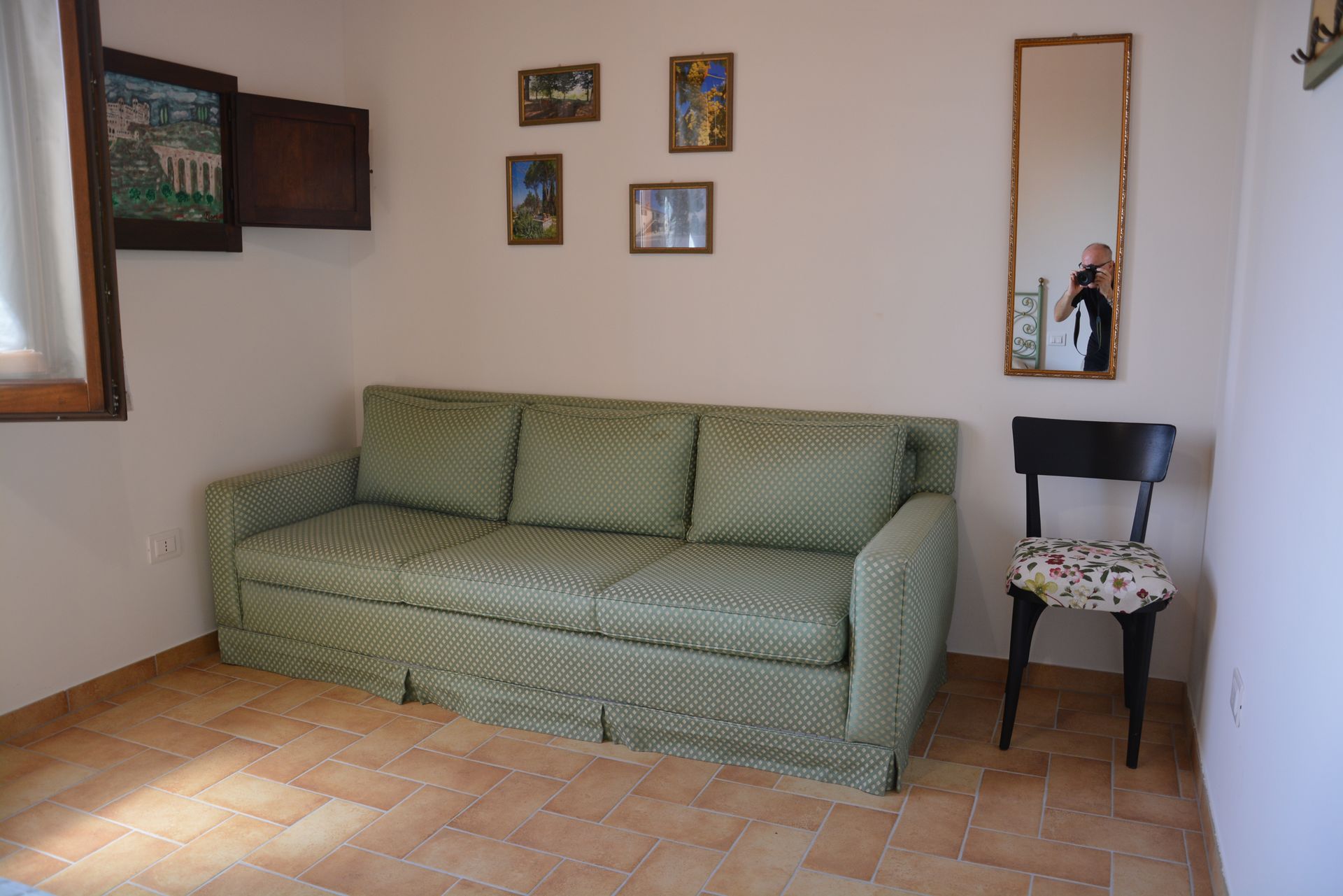 Divano verde in una stanza con quadri e uno specchio. Accanto c'è una sedia nera.