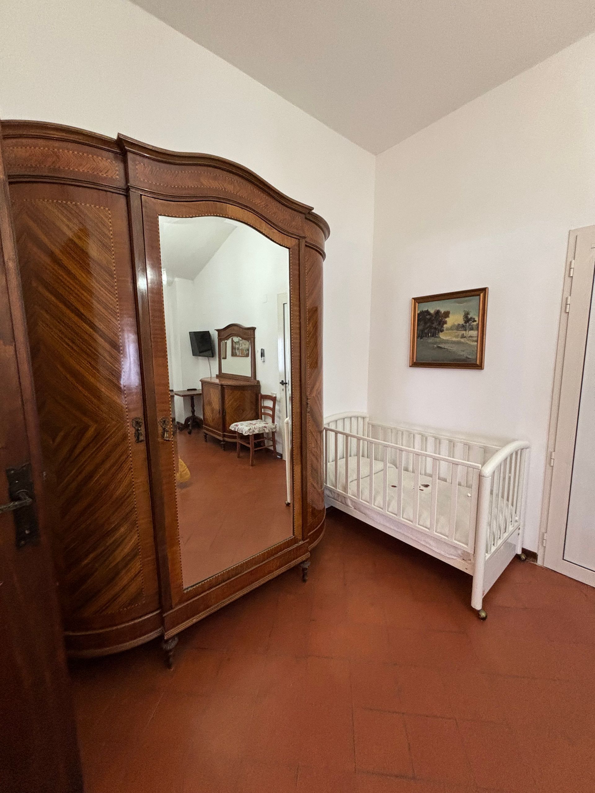 Camera con un grande armadio antico in legno, una culla e un piccolo dipinto su una parete bianca.