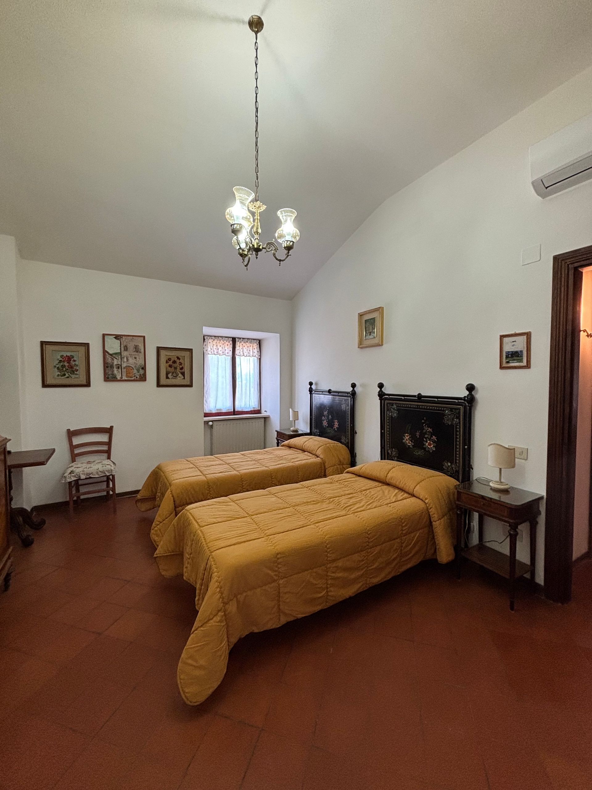 Camera da letto con due letti singoli, coperte gialle, quadri e lampadario decorato.