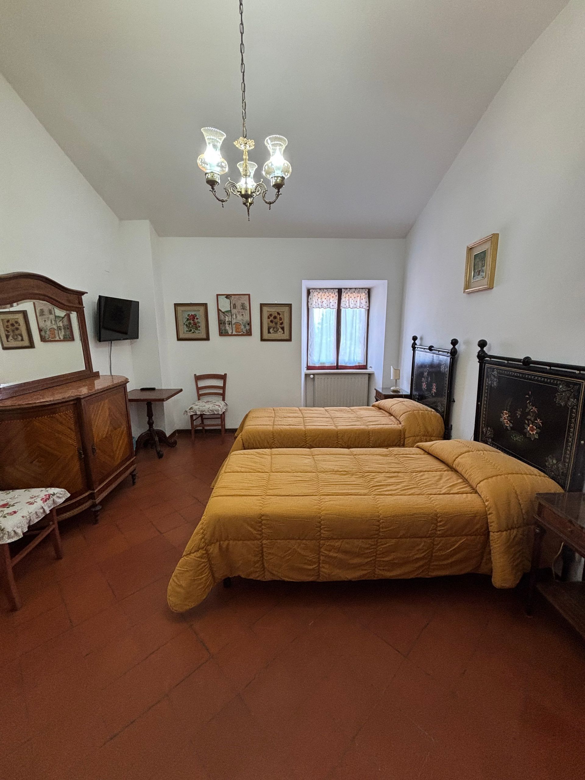 Camera da letto con due letti singoli, mobili antichi e un lampadario; biancheria da letto gialla.