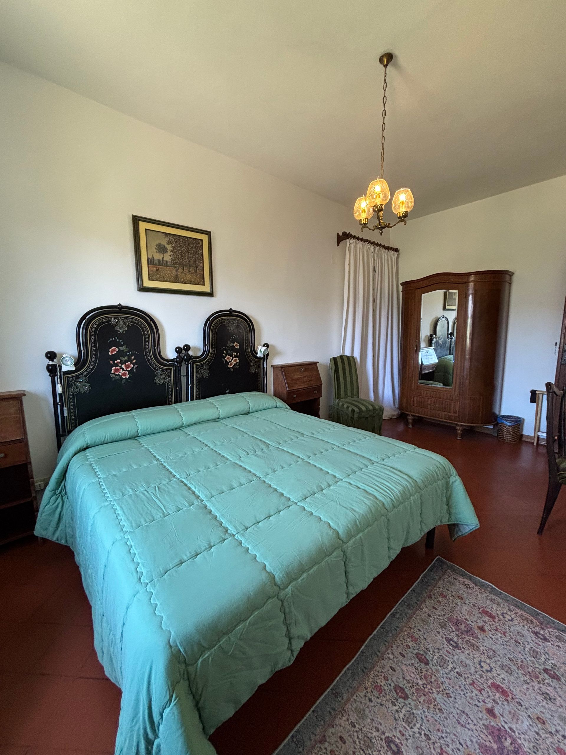 Camera da letto con letto matrimoniale, biancheria da letto verde, mobili antichi e un tappeto su pavimento in piastrelle rosse.