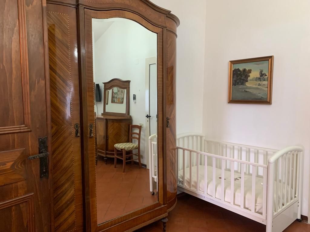 Armadio in legno con specchio, culla bianca e opere d'arte in una camera da letto.