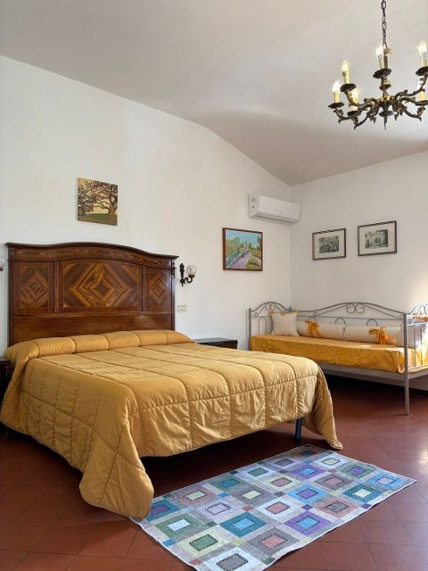 Camera da letto con letto matrimoniale, divano e lampadario; pareti bianche, pavimento rosso.