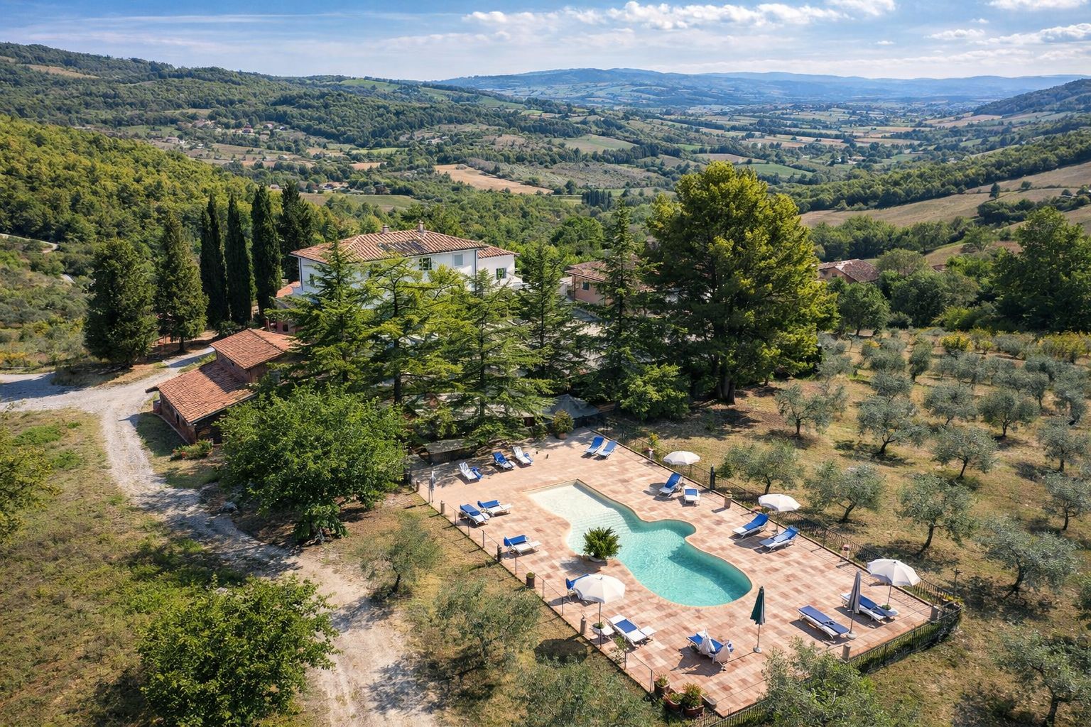 Paesaggio collinare con una casa al tramonto. Campi e alberi punteggiano il paesaggio.