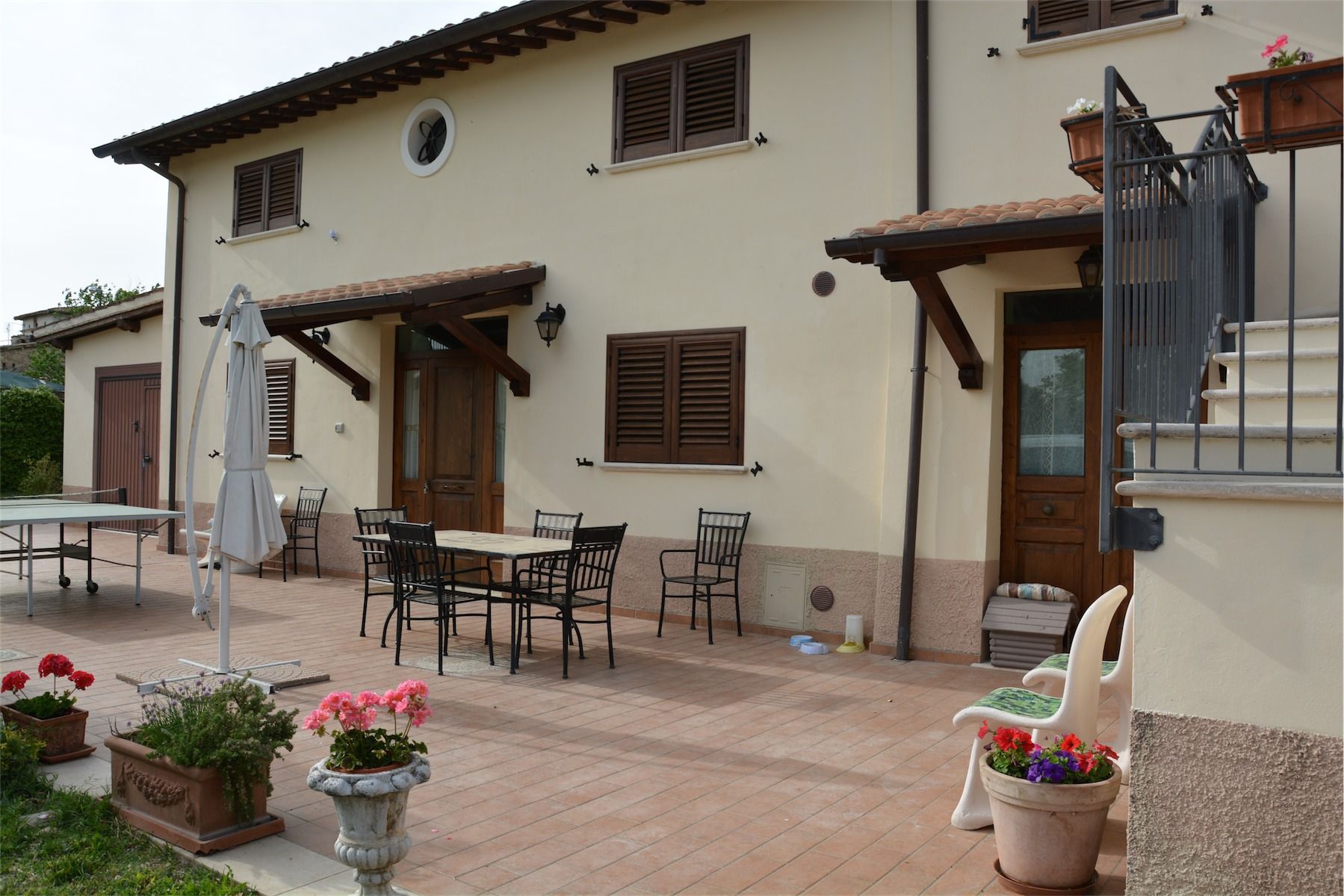 Casa beige a due piani con patio in mattoni, posti a sedere all'aperto e vasi di fiori.