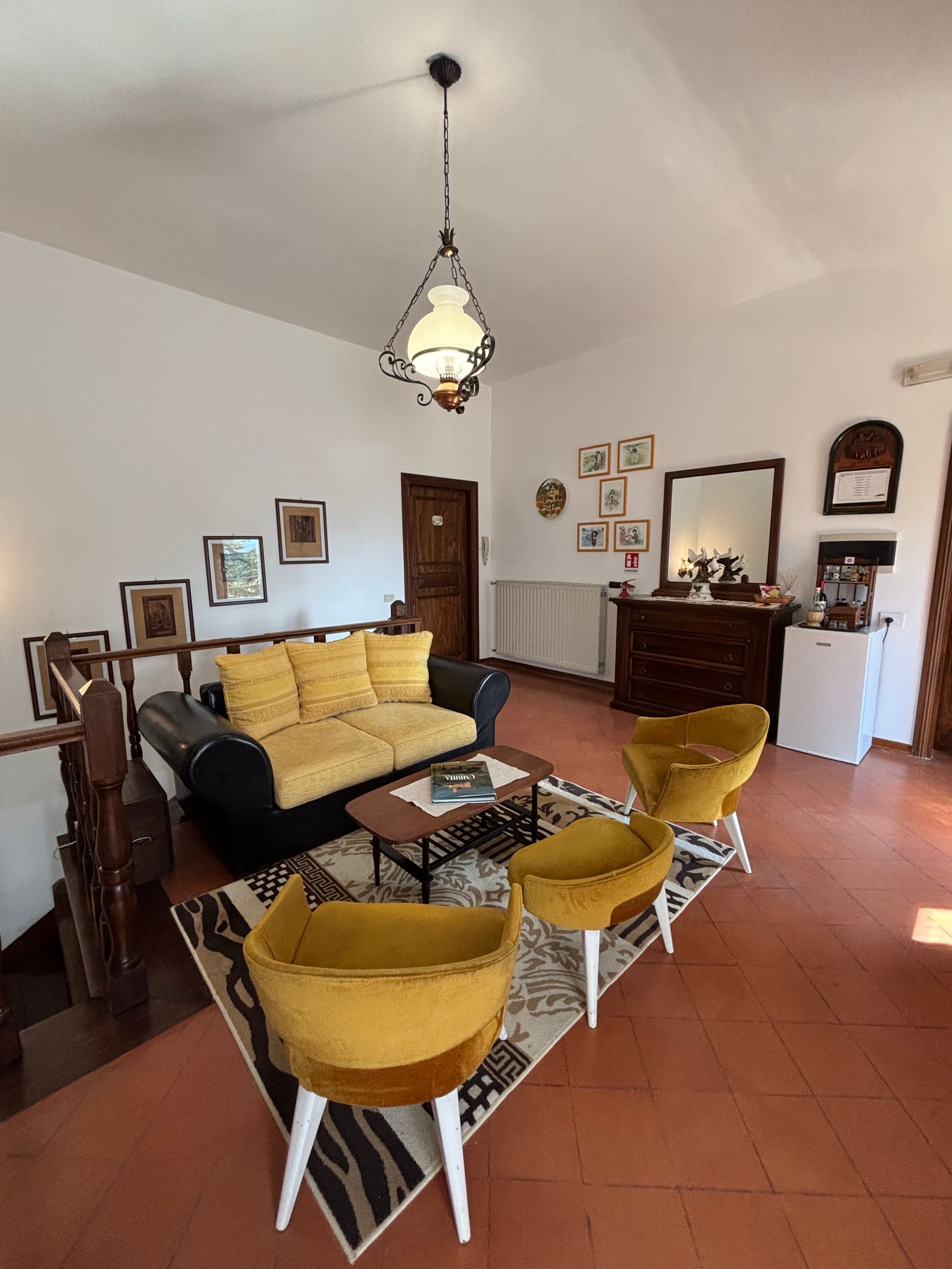Soggiorno con divano e sedie gialle, scala in legno, tappeto decorativo e opere d'arte alle pareti.