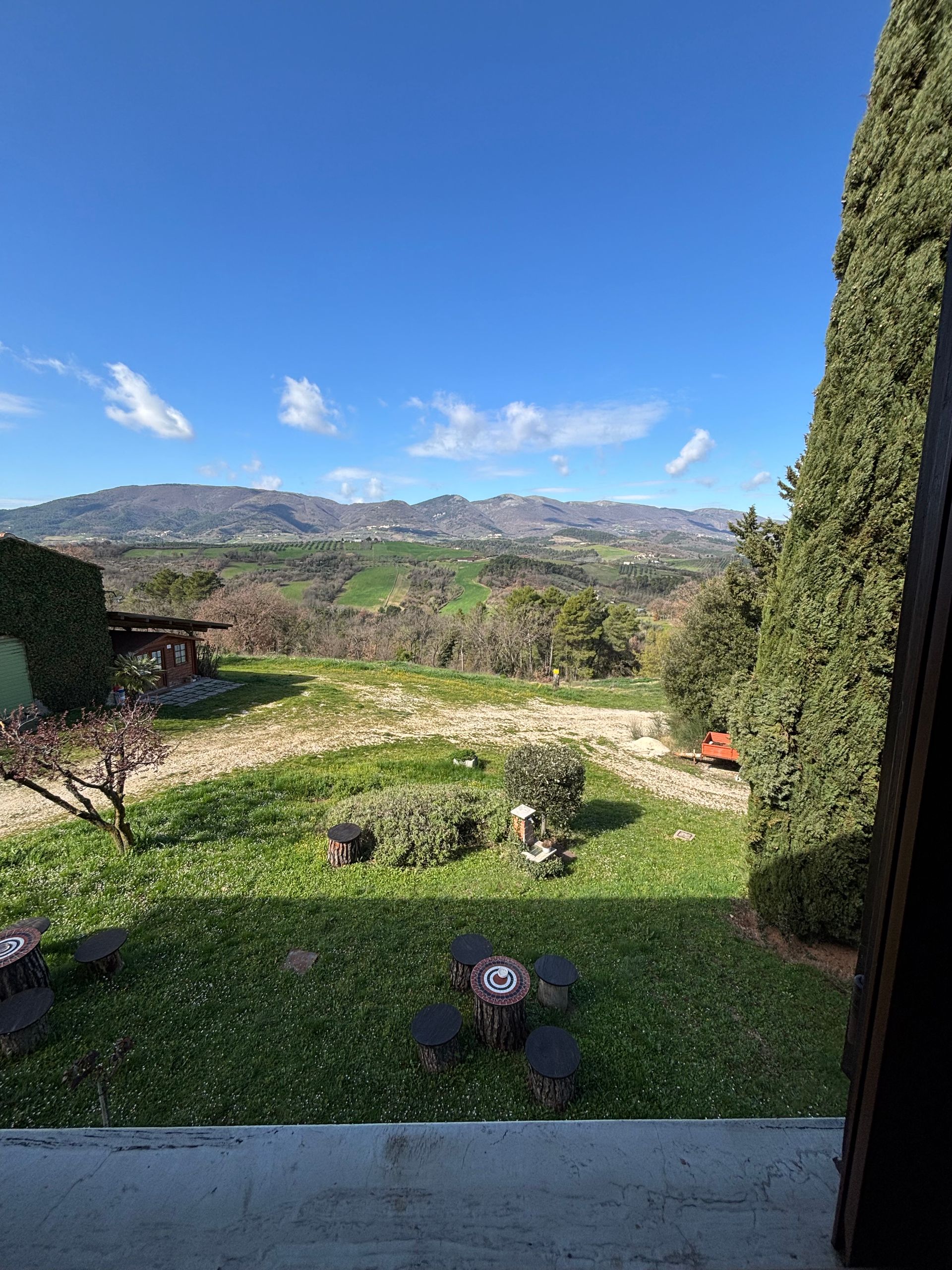 Cortile erboso con vista sulle verdi colline, cielo azzurro e qualche nuvola sparsa.