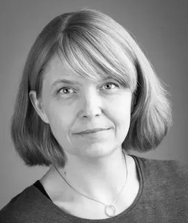 Woman with short blonde hair, in grayscale, smiling slightly, wearing a gray shirt and necklace.