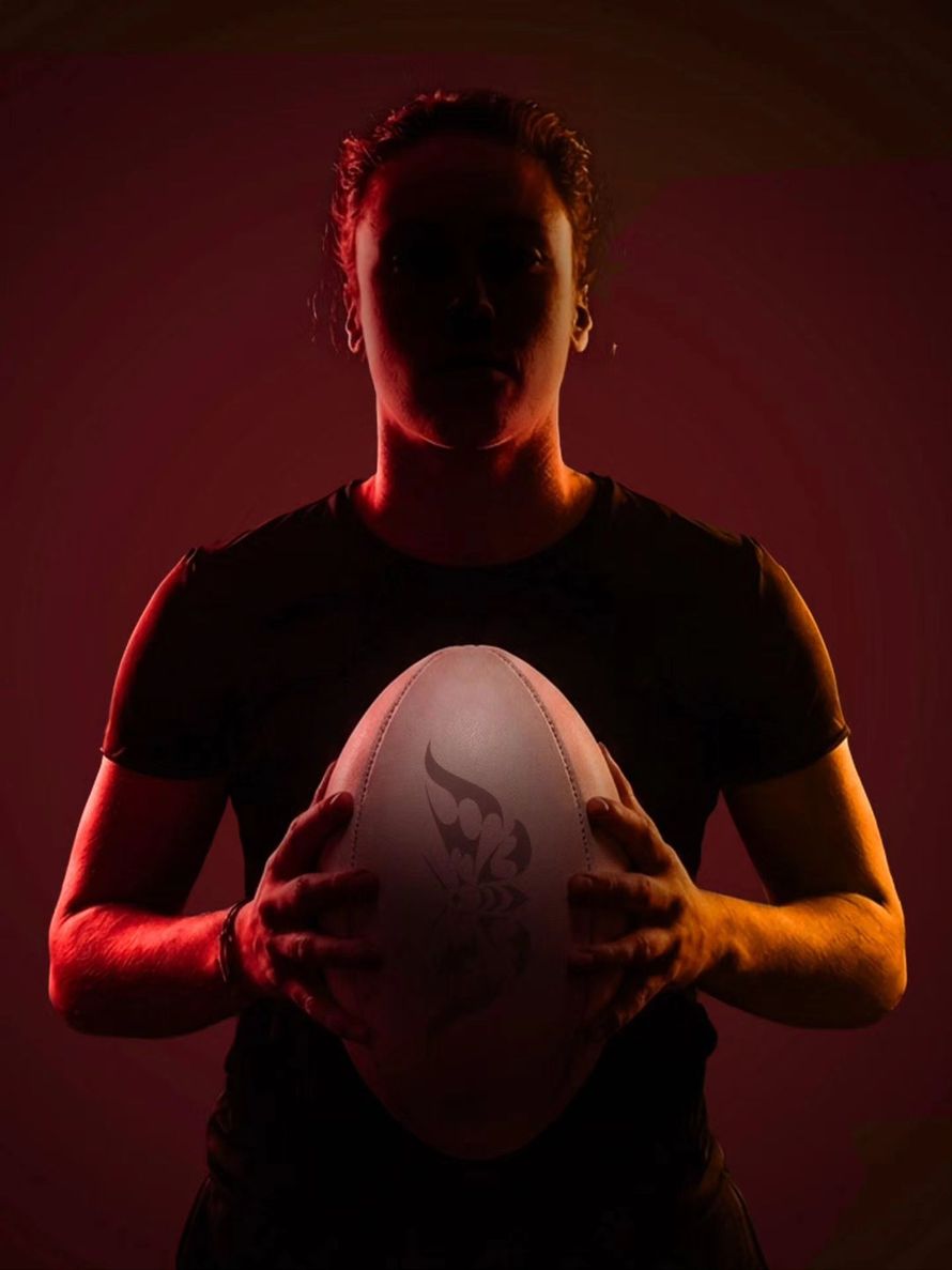 Silhouetted person holding a rugby ball against a dark red background
