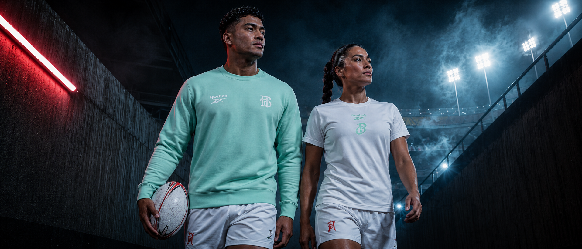 Two soccer players walking in a lit tunnel, one holding a ball, both in training gear