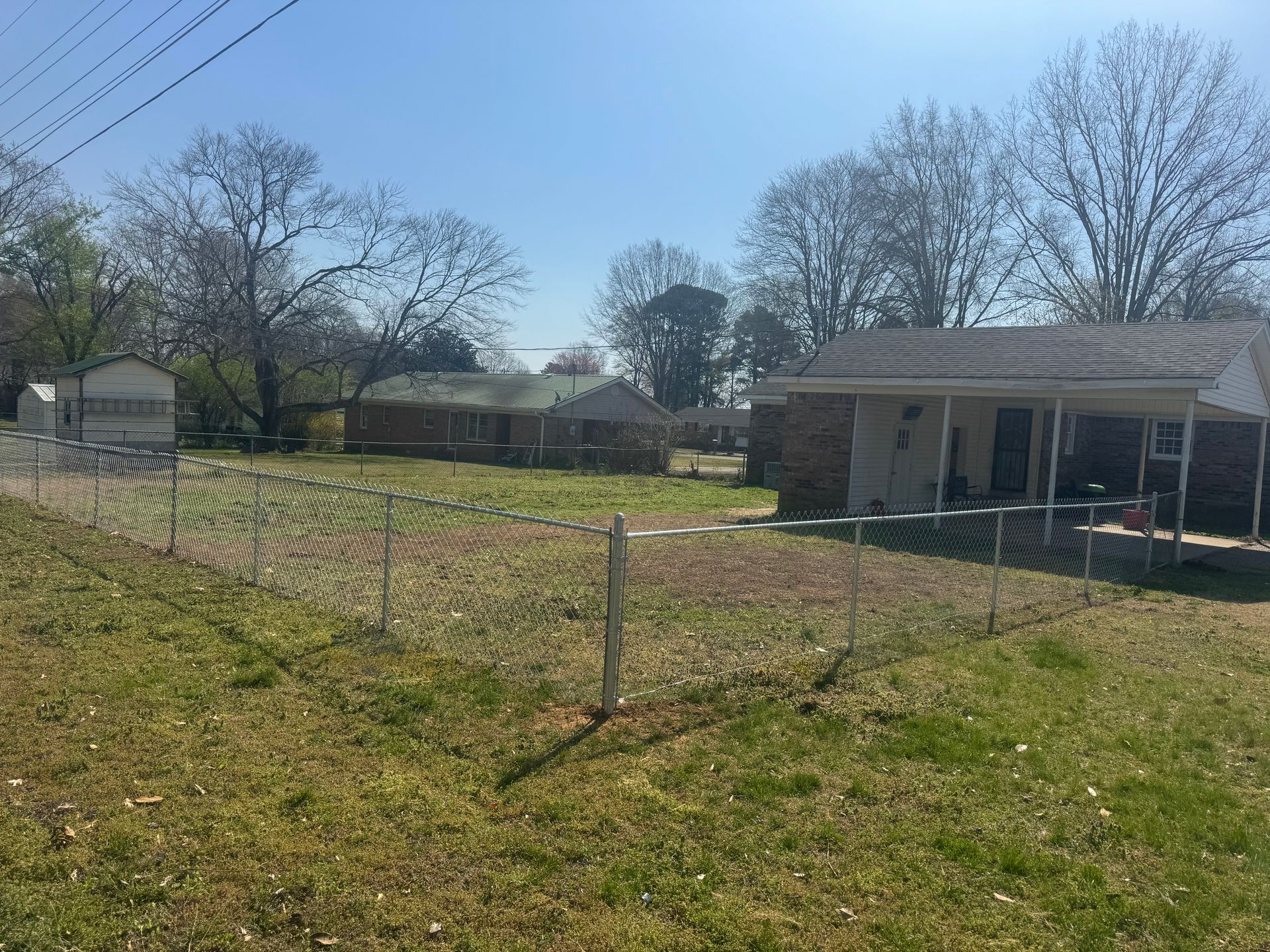 A fenced-in yard with dried grass in front of several single-story residential houses under a clear blue sky.
