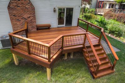 A wooden deck with stairs and railings in front of a house.