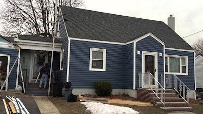 A blue house with a black roof is being painted.