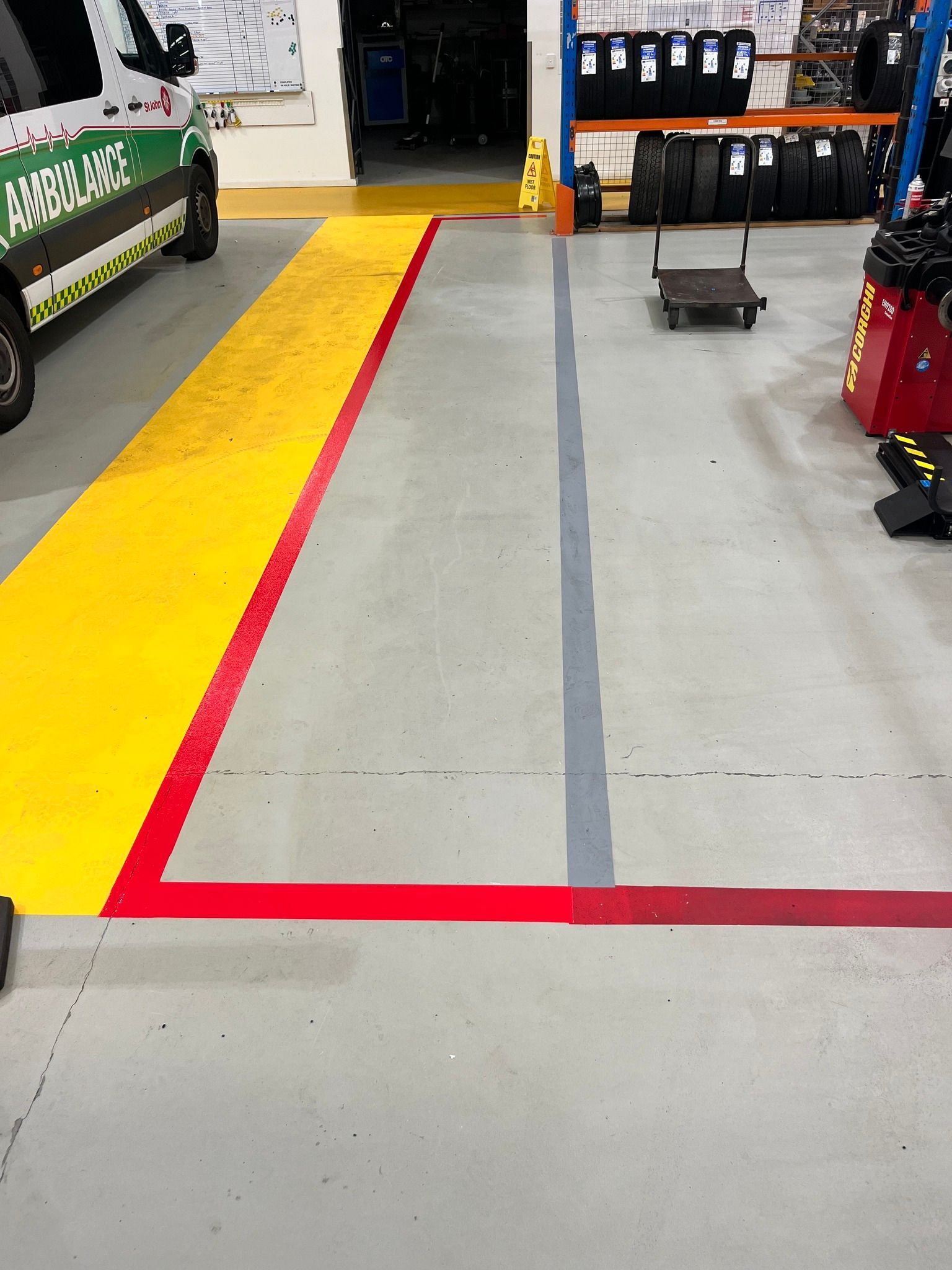 Floor markings in an automotive shop: yellow, red, and gray lines define spaces for vehicles, equipment, and work areas.