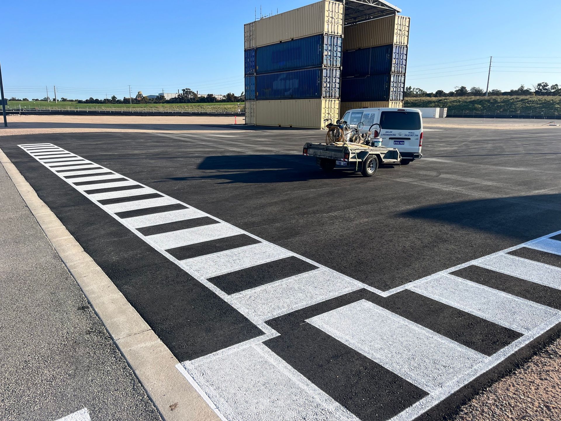 Asphalt lot with a white and black pattern, a vehicle, and stacked shipping containers.