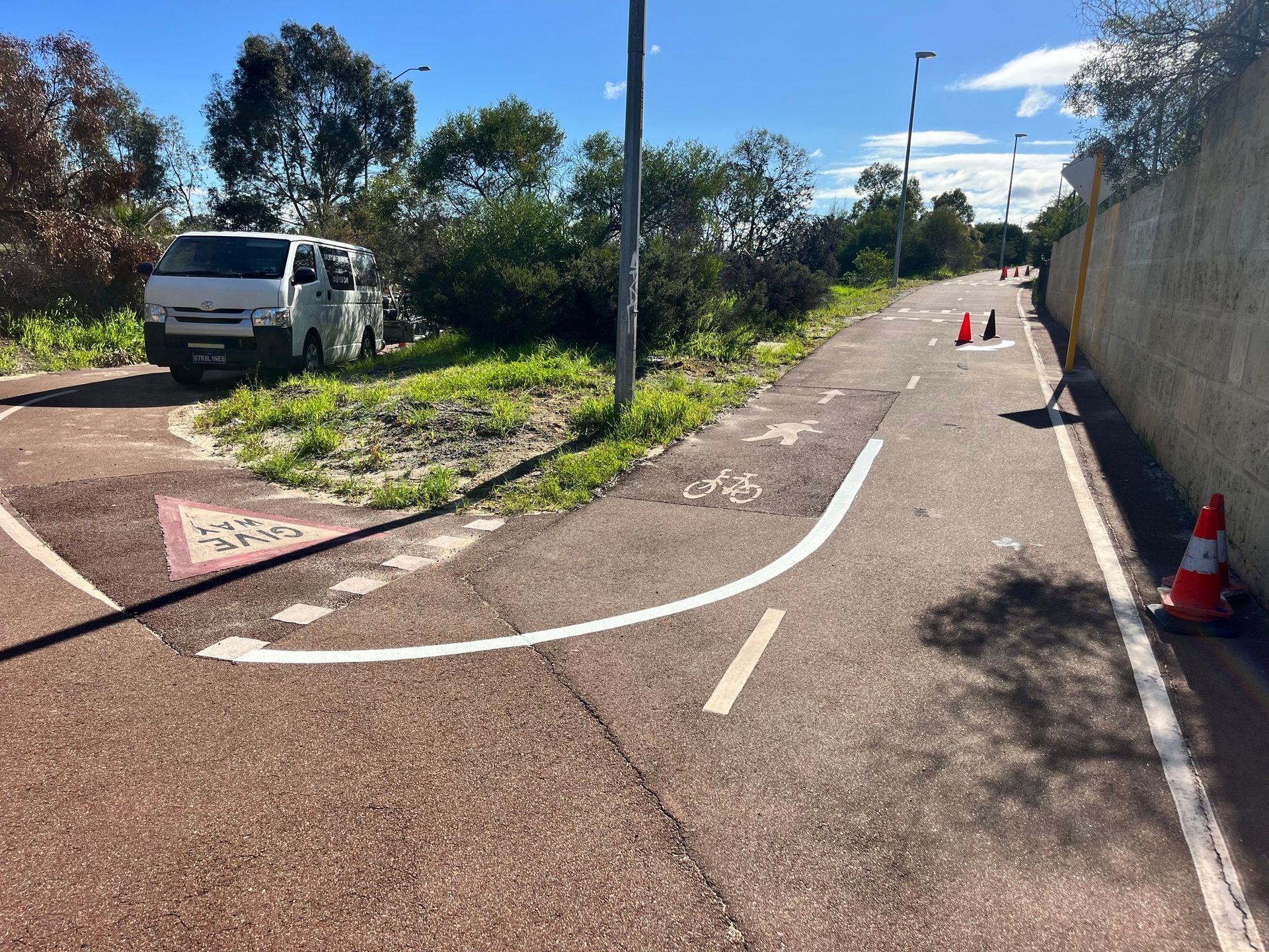 A paved path curves, bordered by a wall and grassy area. A white van is parked nearby.