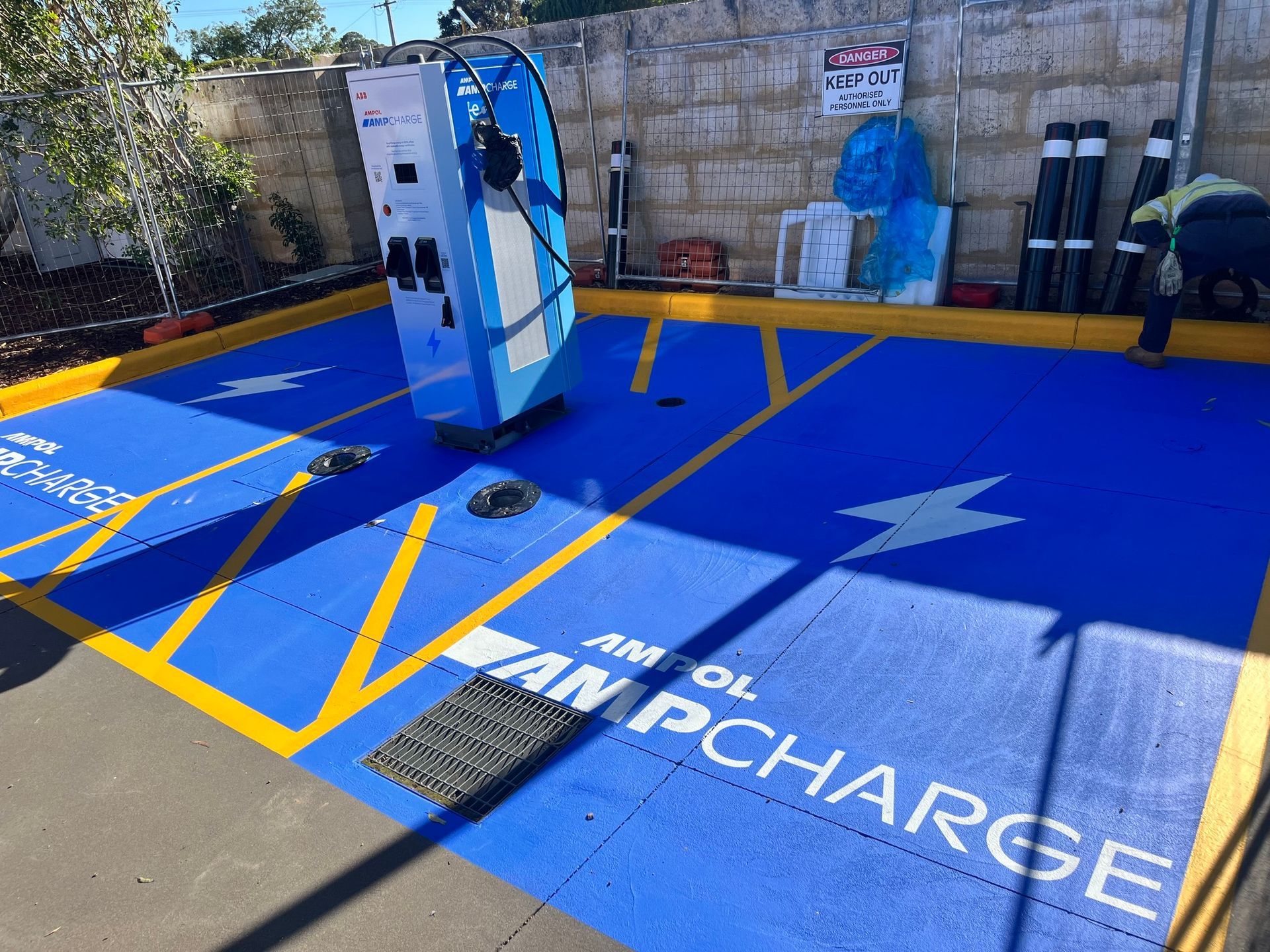 Electric vehicle charging station with blue AMPOL AMPCHARGE pavement, yellow markings, and a charging unit.