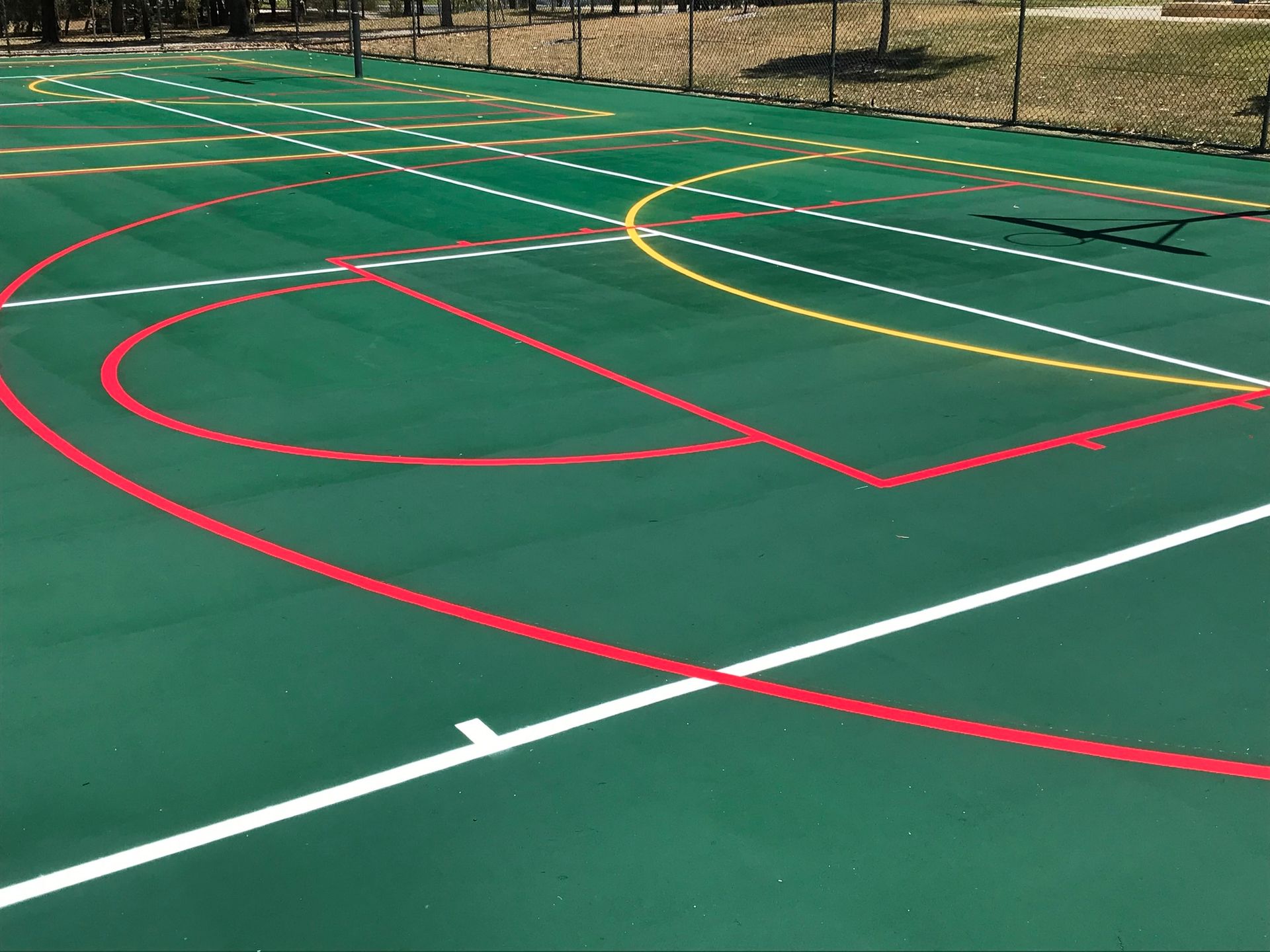 Green outdoor sports court with white, red, and yellow lines, possibly for basketball and other activities.