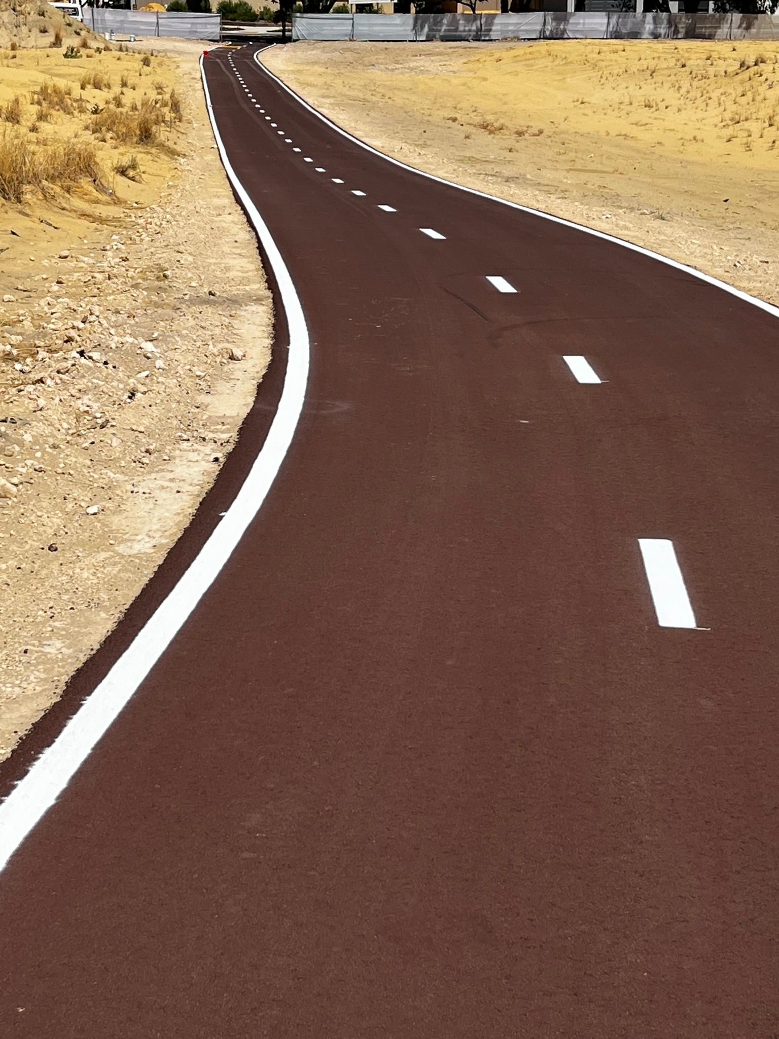 Brown asphalt path with white lane markings winding through a dry, tan landscape.