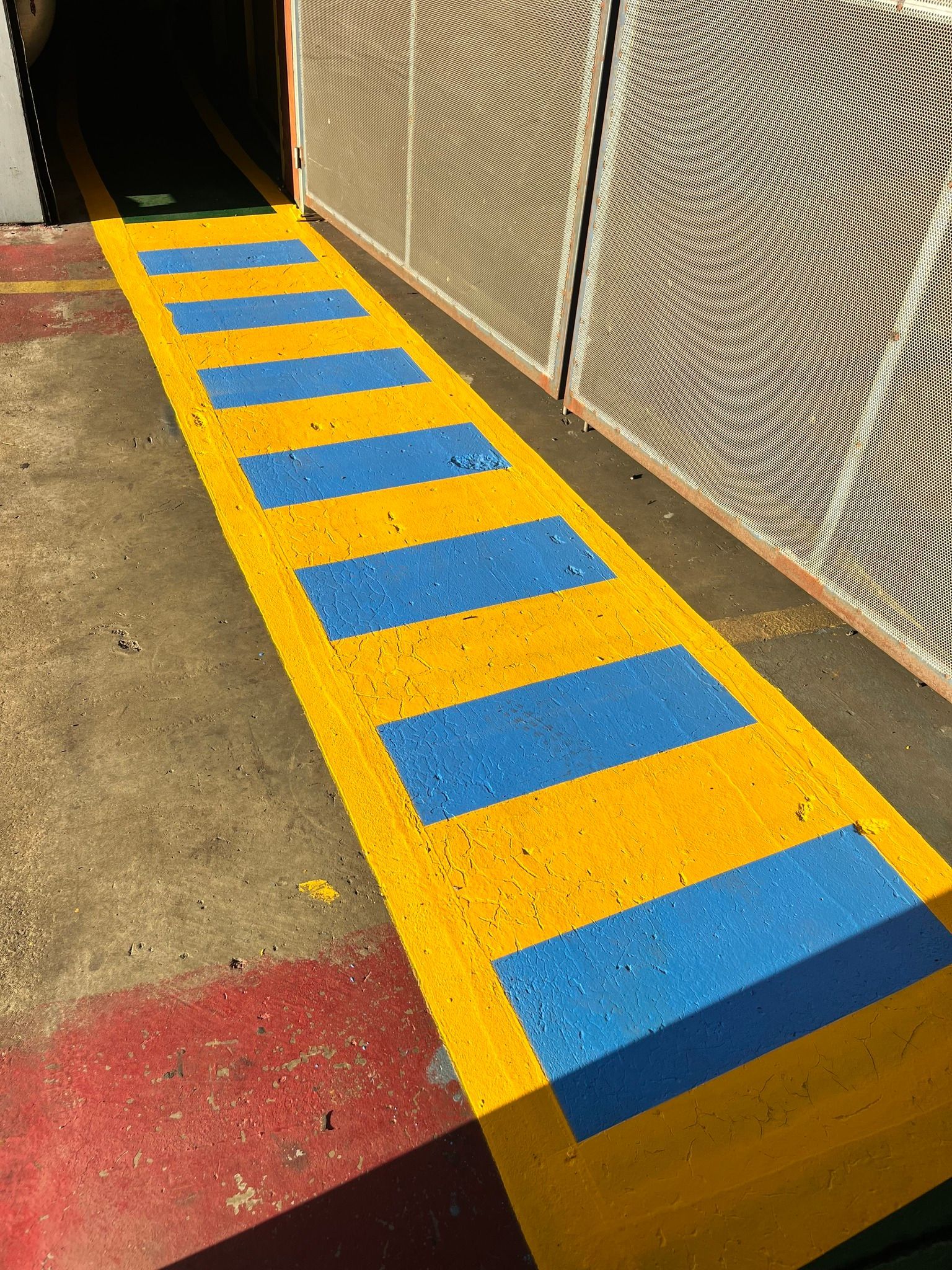 Yellow and blue striped ramp leading to a doorway, set against a concrete surface.