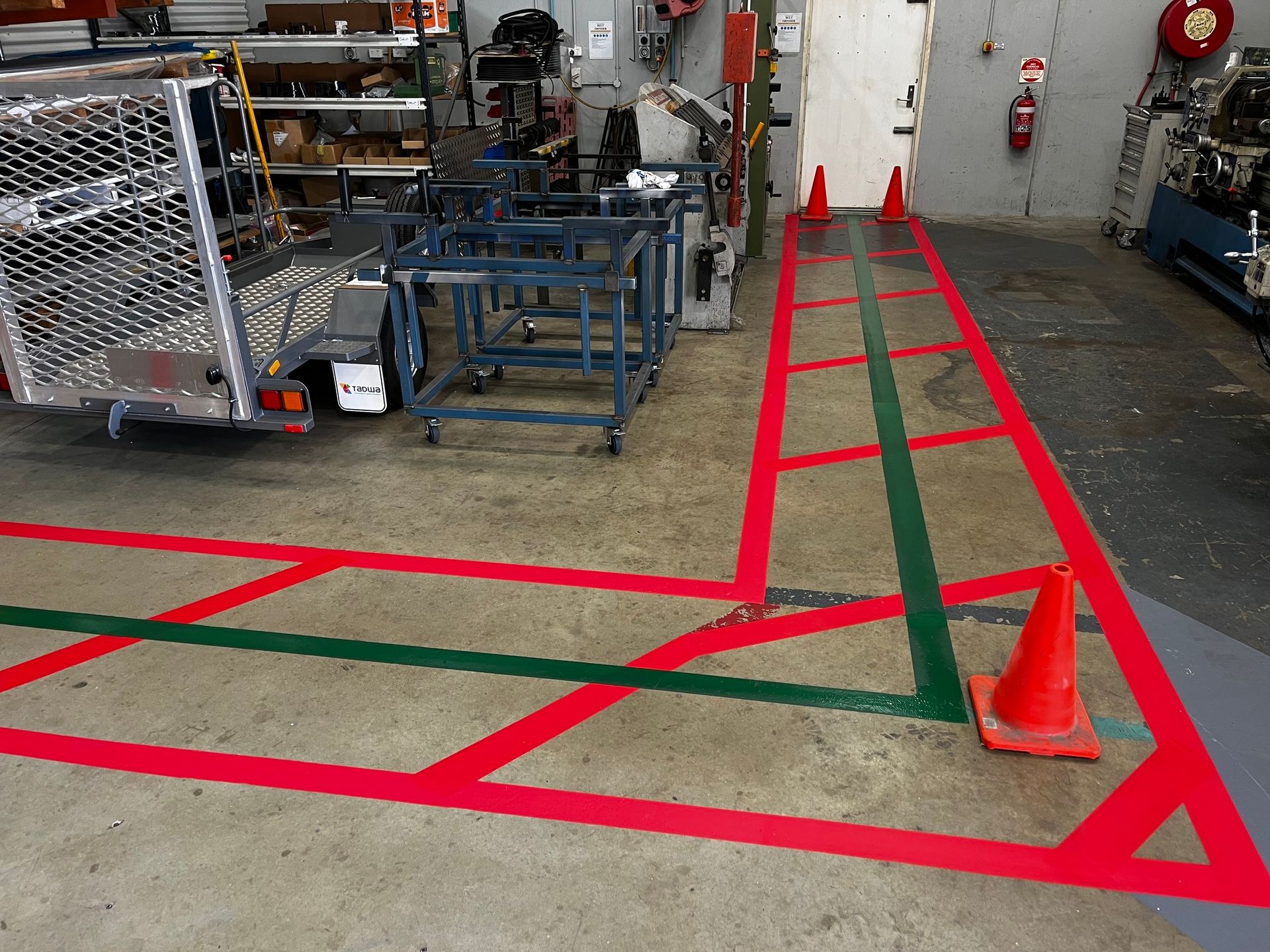 Factory floor with red and green painted lines. Cones mark a path. Equipment and machinery are in the background.