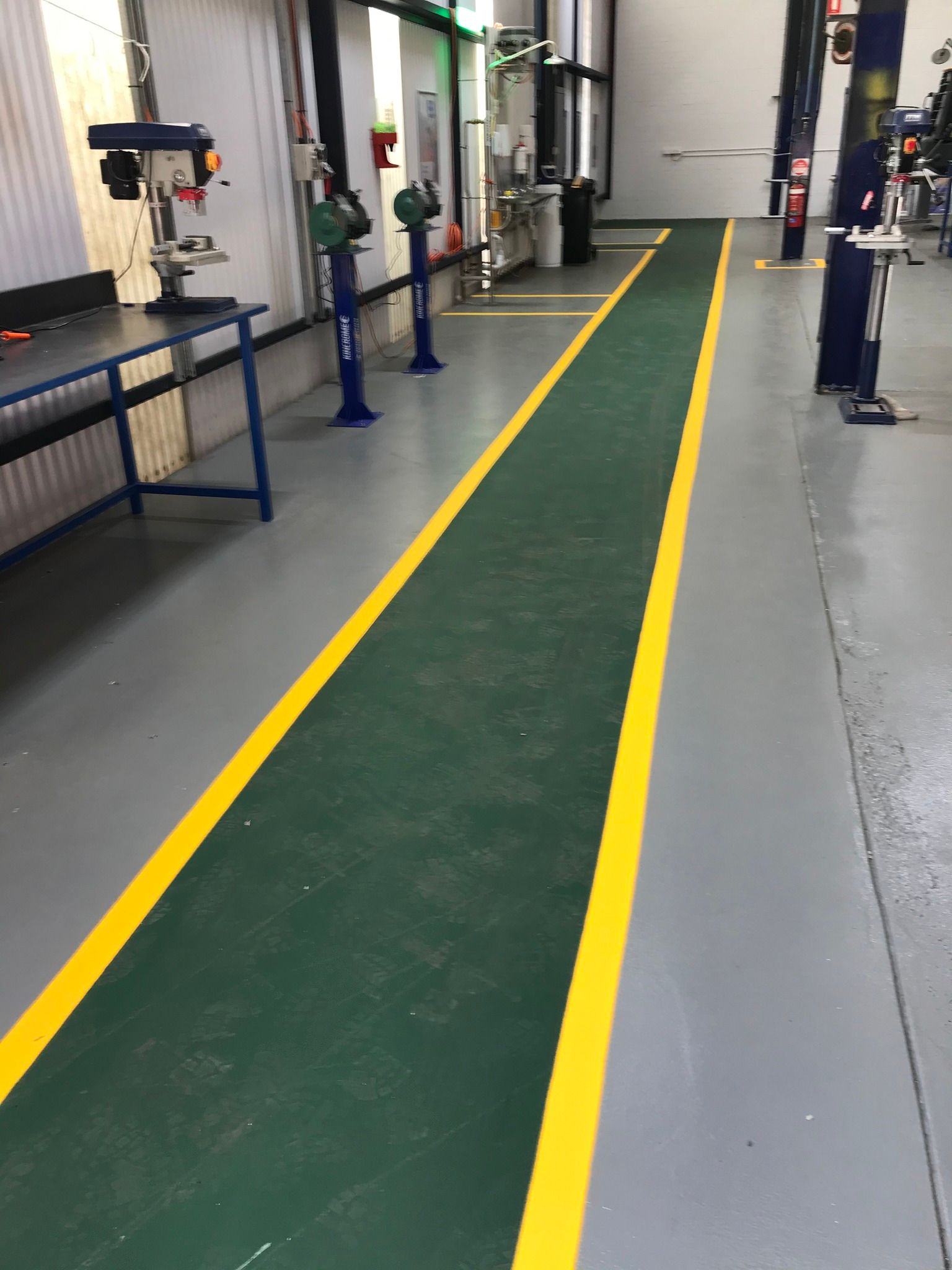 Green floor walkway with yellow lines in an industrial setting.