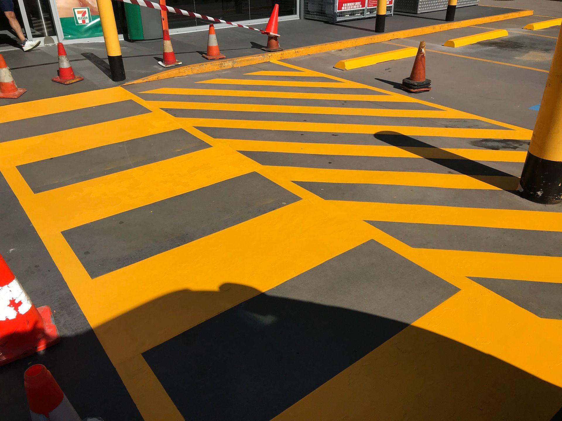 Yellow and black hazard markings on pavement with orange traffic cones.