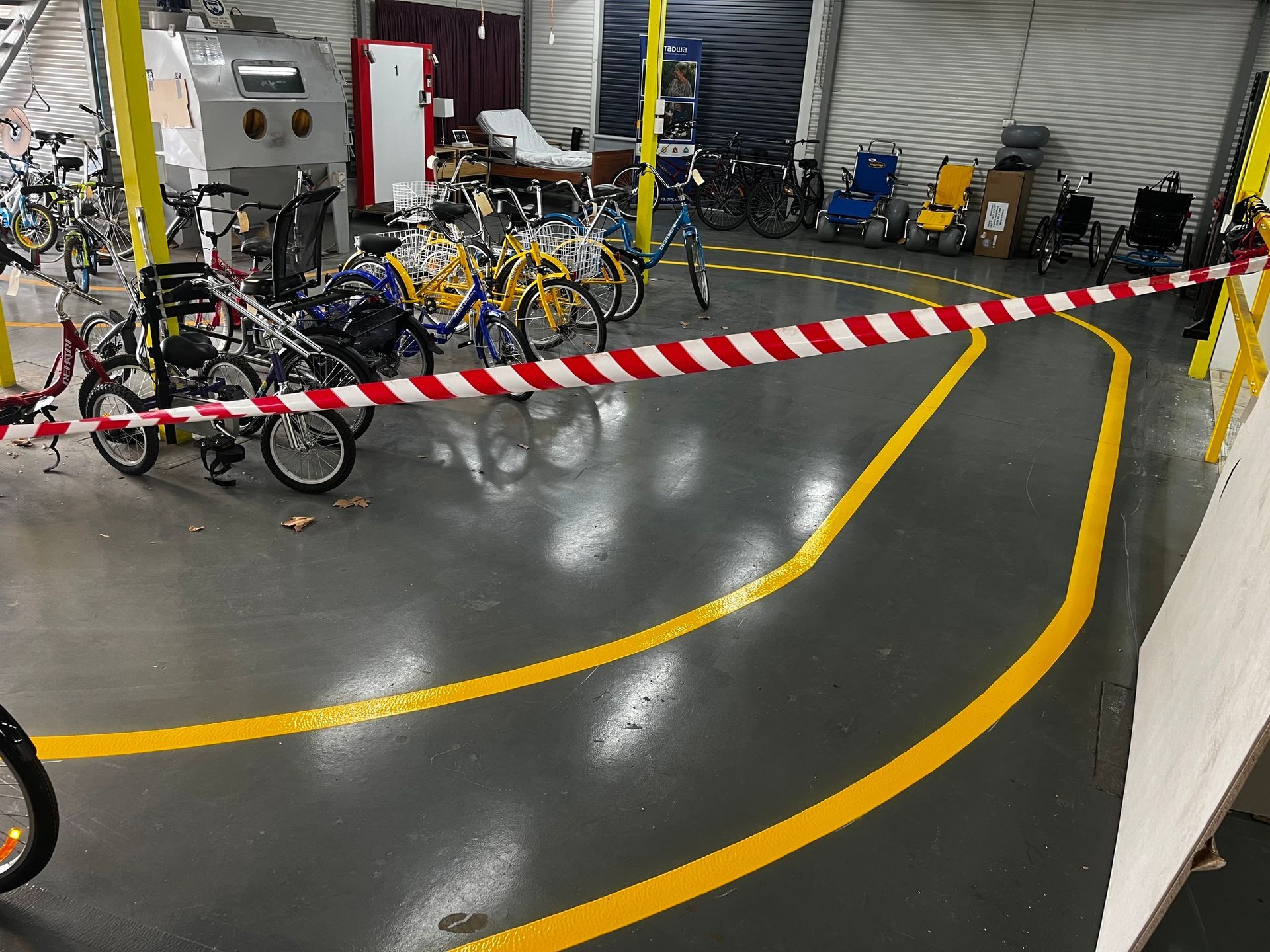 Garage with yellow-lined path and caution tape, various bikes and mobility devices.