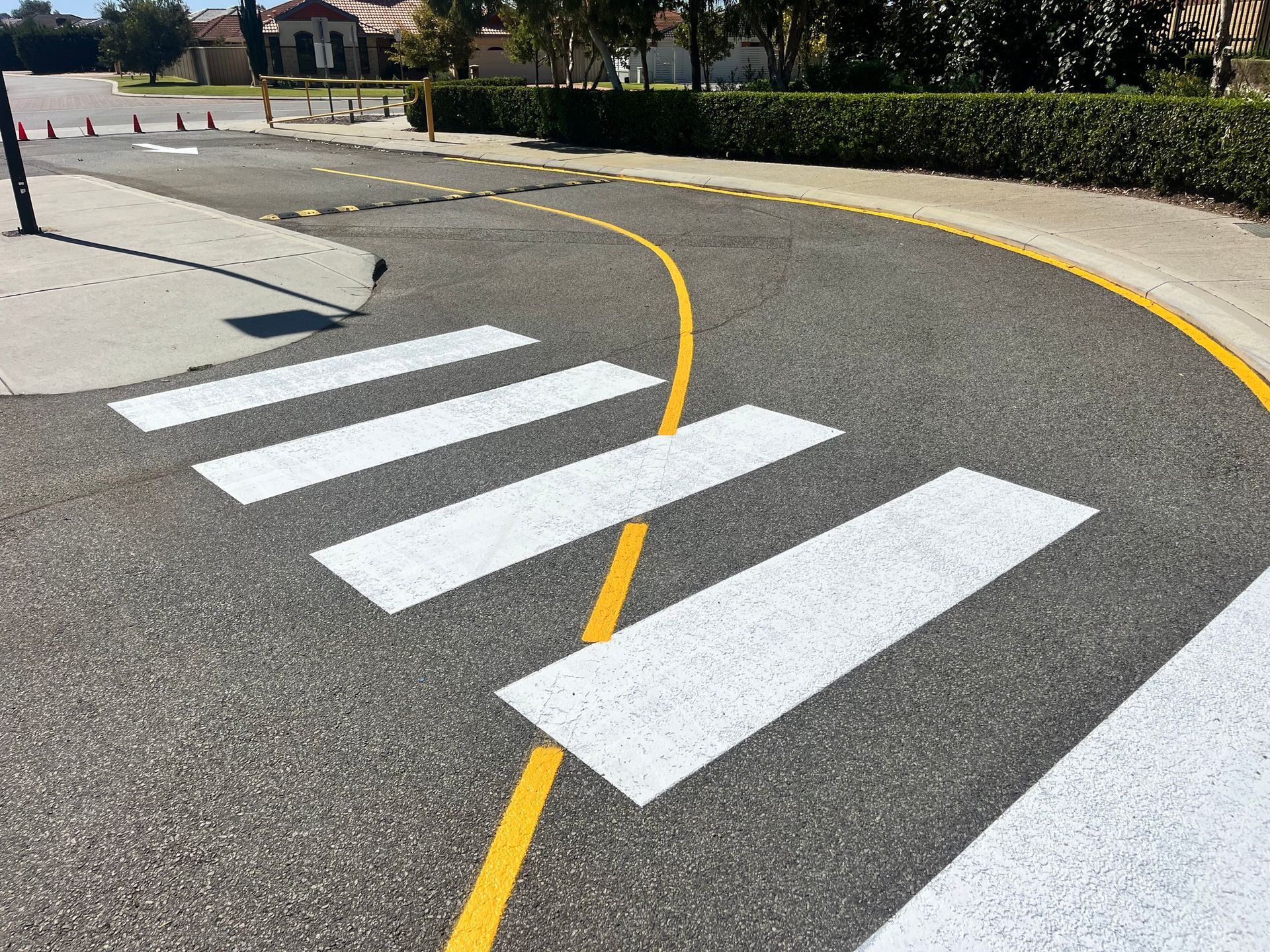 Crosswalk on curved asphalt road with yellow lines, white stripes, and curb.