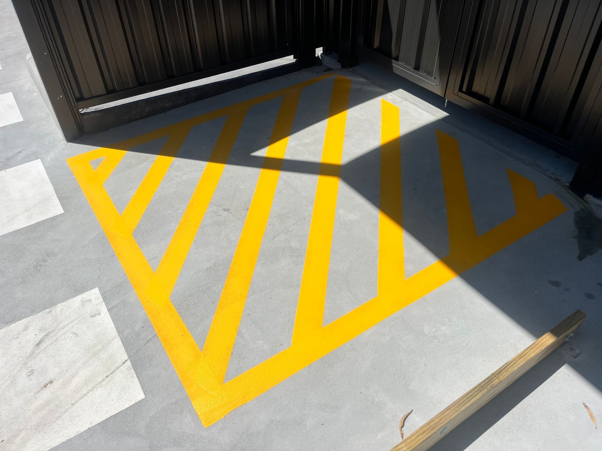 Yellow striped pavement markings in front of a dark gate, indicating a restricted area.